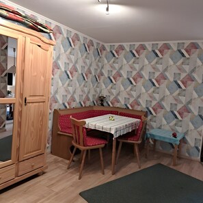 Un coin repas avec un buffet en bois, une table recouverte d’une nappe à carreaux et un papier peint à motifs.