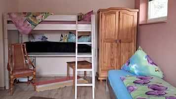 Een slaapkamer met stapelbedden, een houten garderobe, een stoel, een klein tafeltje en een raam.