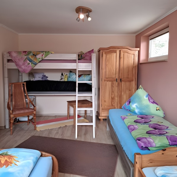 A bedroom with bunk beds, a wooden wardrobe, a chair, a small table, and a window.