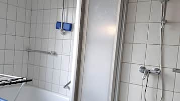 A bathroom with white tiled walls, a shower with a handheld showerhead, and a towel rack with blue towels.