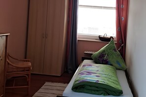 Une chambre à coucher avec un lit, une chaise, une armoire et une fenêtre avec des rideaux.