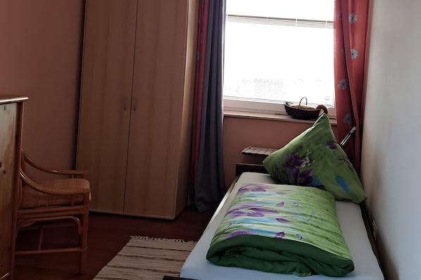 A bedroom with a bed, a chair, a wardrobe, and a window with curtains.