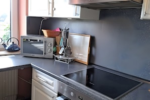 A kitchen with a microwave, kettle, and a black induction cooktop.