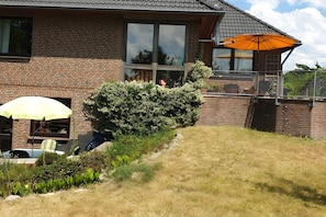 A brick house with a large window, a patio with a yellow umbrella, and a well-maintained garden.