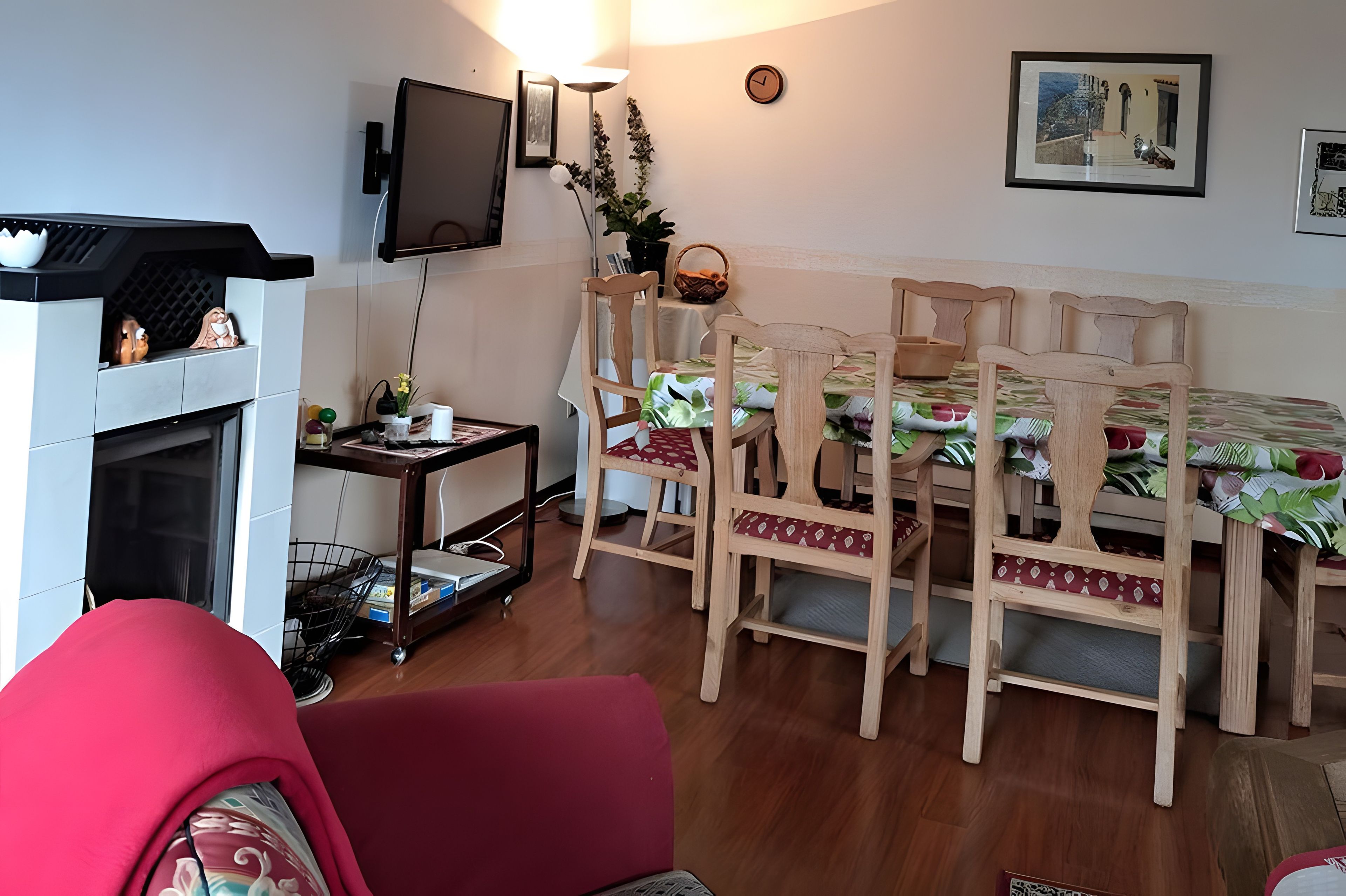 Ein Zimmer mit Kamin, einem an der Wand befestigten Fernseher, einem Esstisch mit Stühlen und einer Uhr.