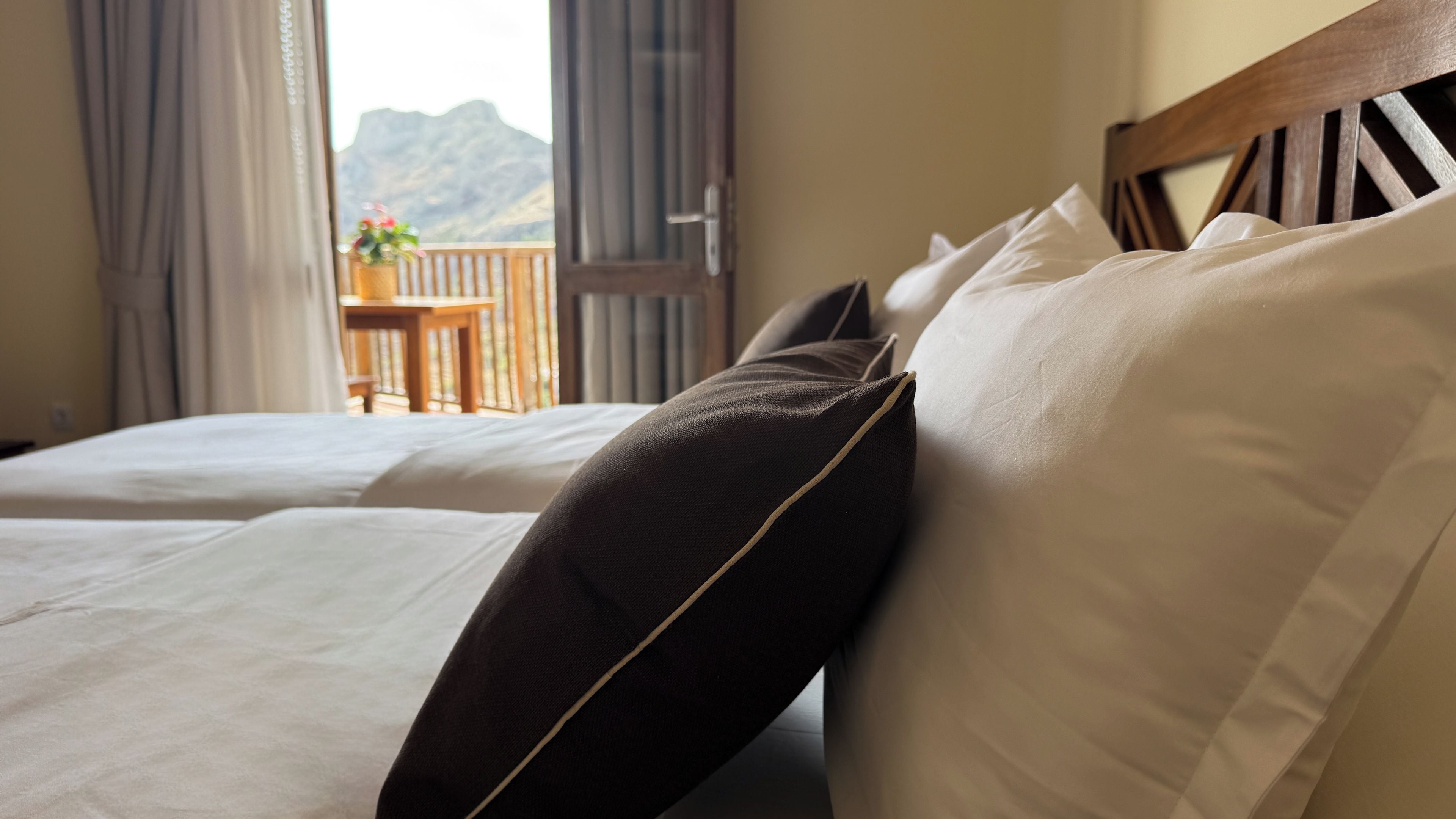 Quarto de hotel com cama, cabeceira de madeira e vista para montanhas pela janela.