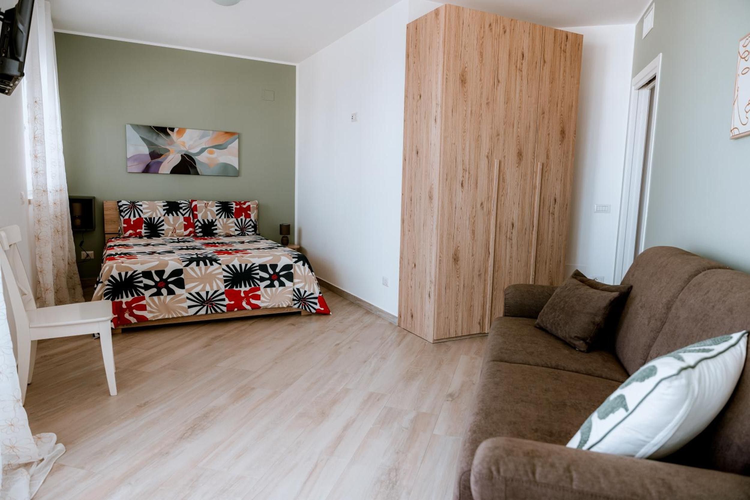 A bedroom with a bed, a wooden wardrobe, a brown sofa, and a chair.