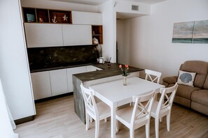 Une cuisine moderne avec des meubles blancs, un plan de travail foncé et un coin repas comprenant une table et des chaises blanches.