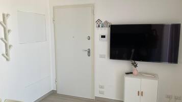 Ett rum med en vit dörr, en platt-TV som är monterad på väggen, ett litet skåp med en vas och en stol.