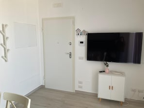 Ett rum med en vit dörr, en platt-TV som är monterad på väggen, ett litet skåp med en vas och en stol.