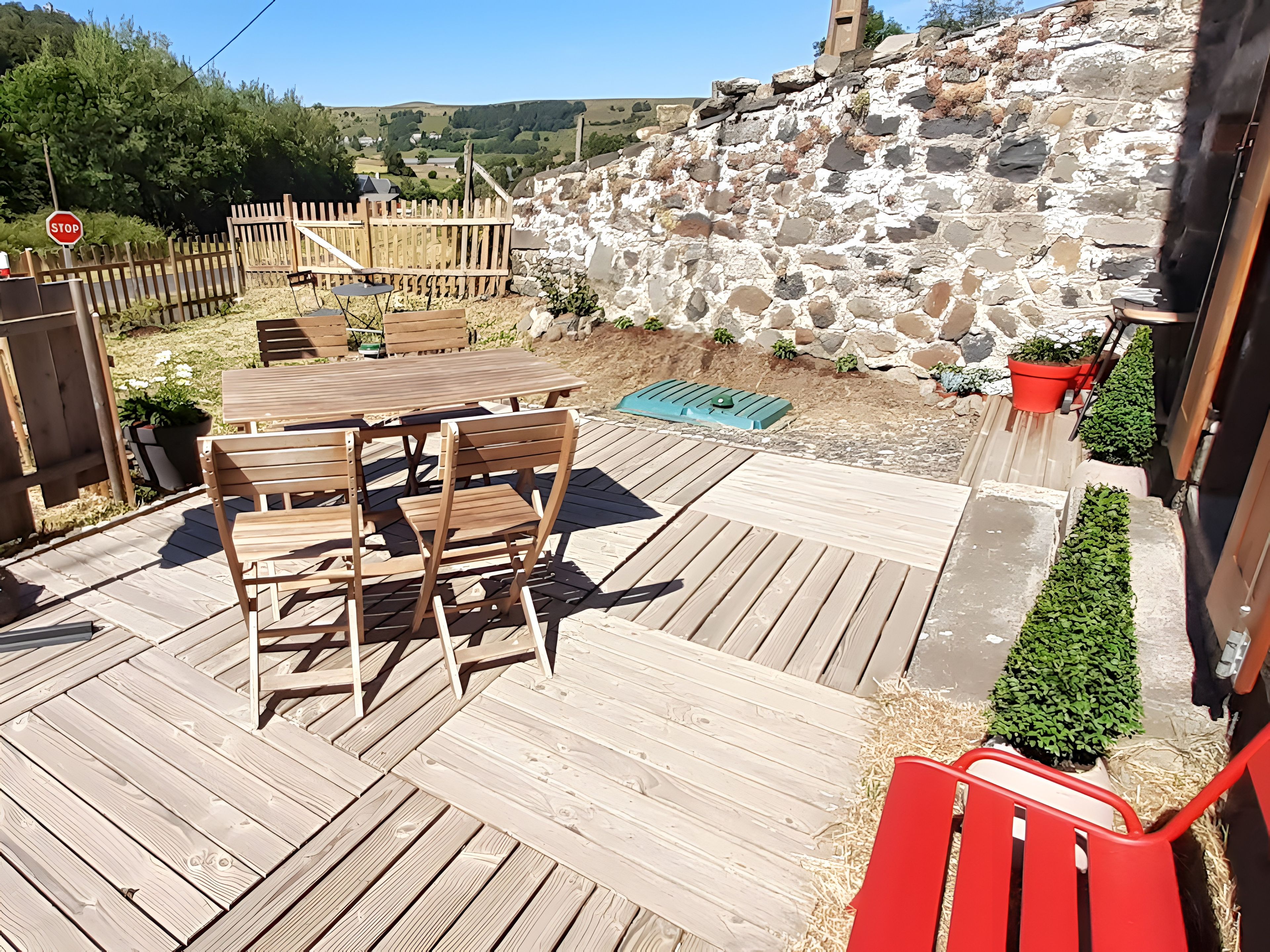 Eine Holzterrasse mit Tisch und Stühlen, umgeben von einer Steinmauer und einem Holzzaun.