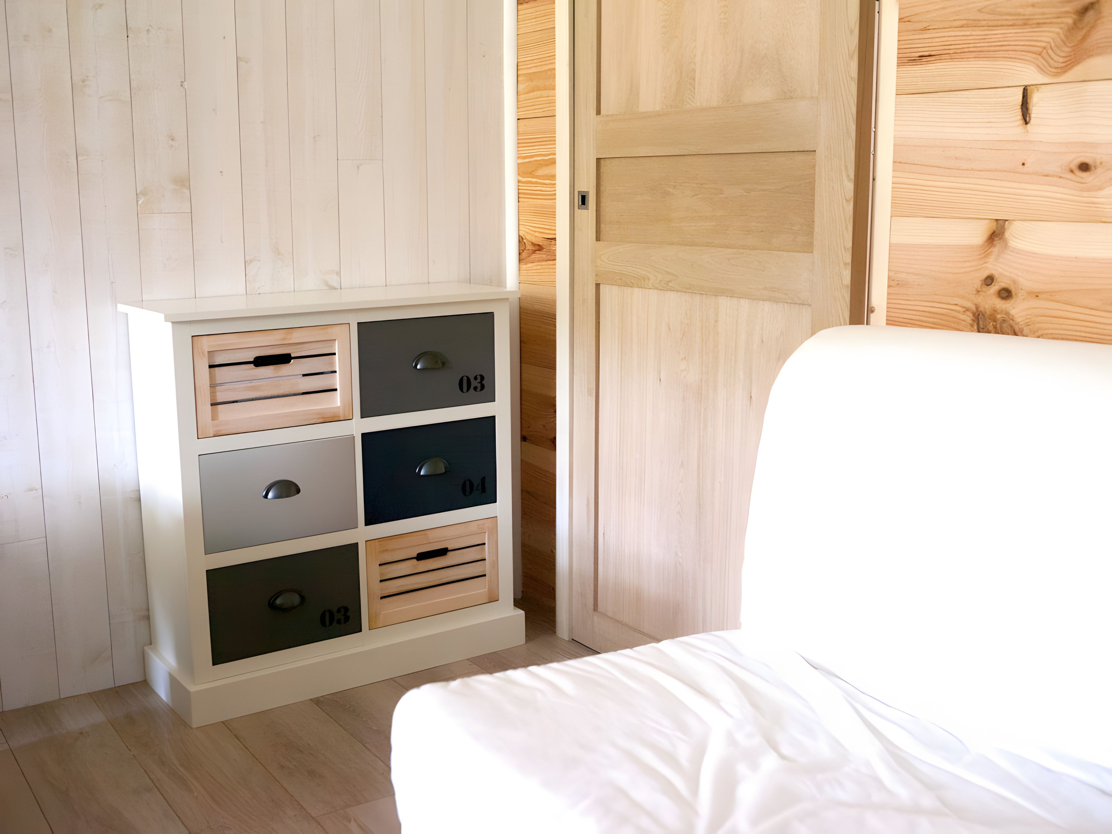 Quarto com uma cama, guarda-roupa de madeira com gavetas e porta de madeira.