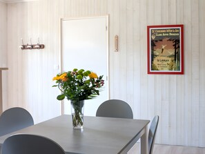 A dining area with a table, chairs, a vase with flowers, a door, and a framed poster on the wall.