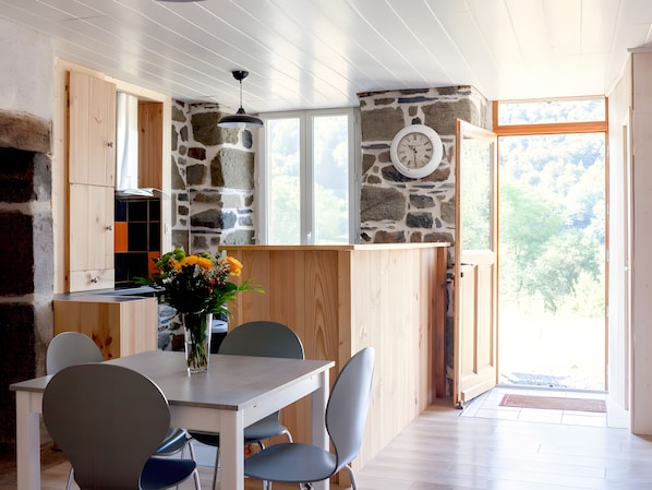 Un coin repas comprenant une table, des chaises, un vase avec des fleurs, une horloge au mur et un mur en pierre.