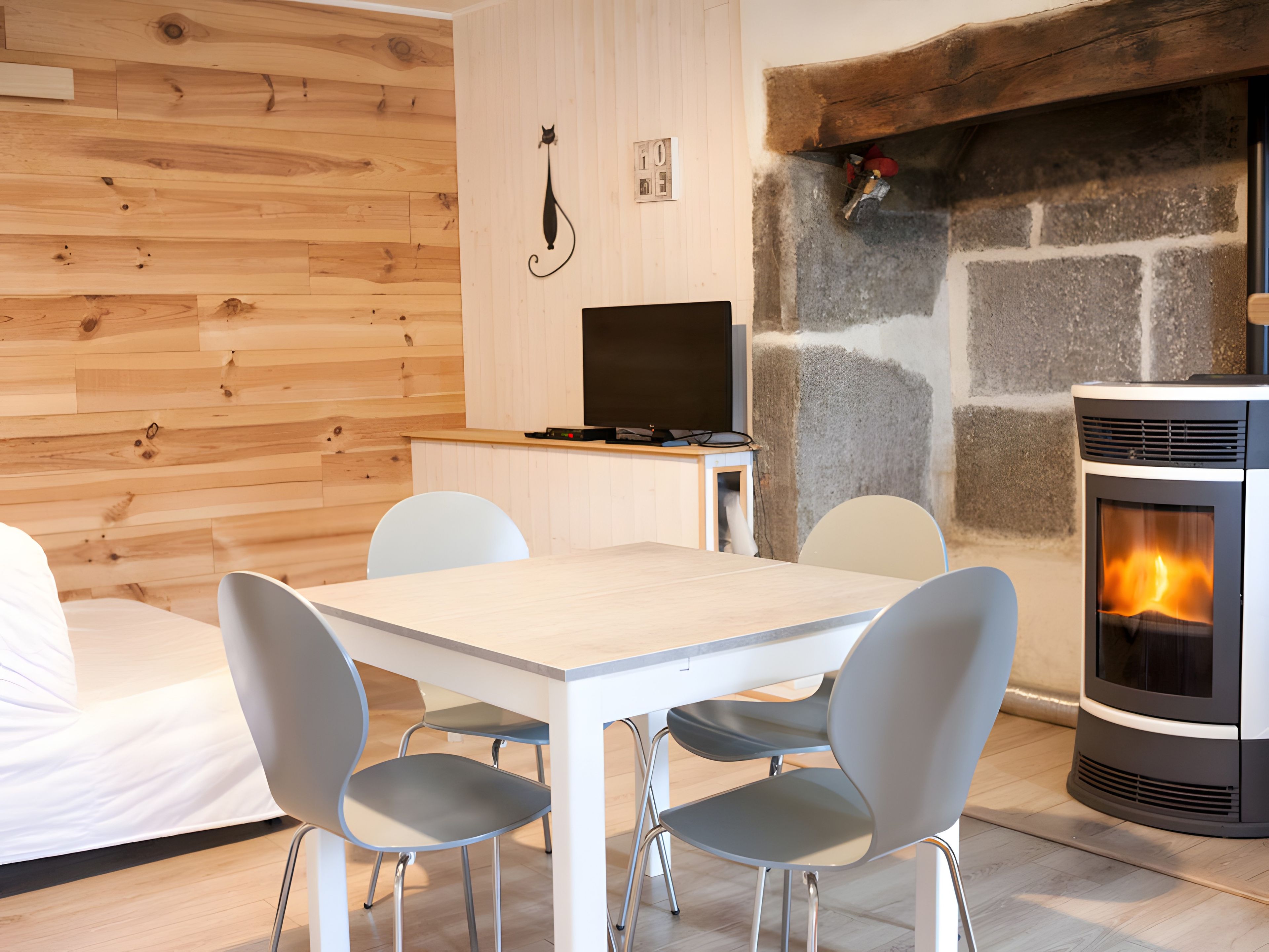 Uma sala de estar moderna com lareira de pedra, televisão e área de jantar com cadeiras e mesa.