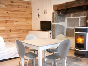 Ein modernes Wohnzimmer mit Kamin aus Stein, einem Fernseher und einem Essbereich mit Stühlen und einem Tisch.