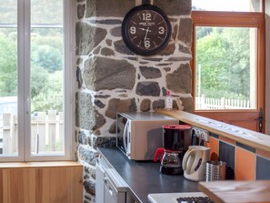A kitchen with a stone wall, a clock, a coffee maker, and a view of greenery outside.