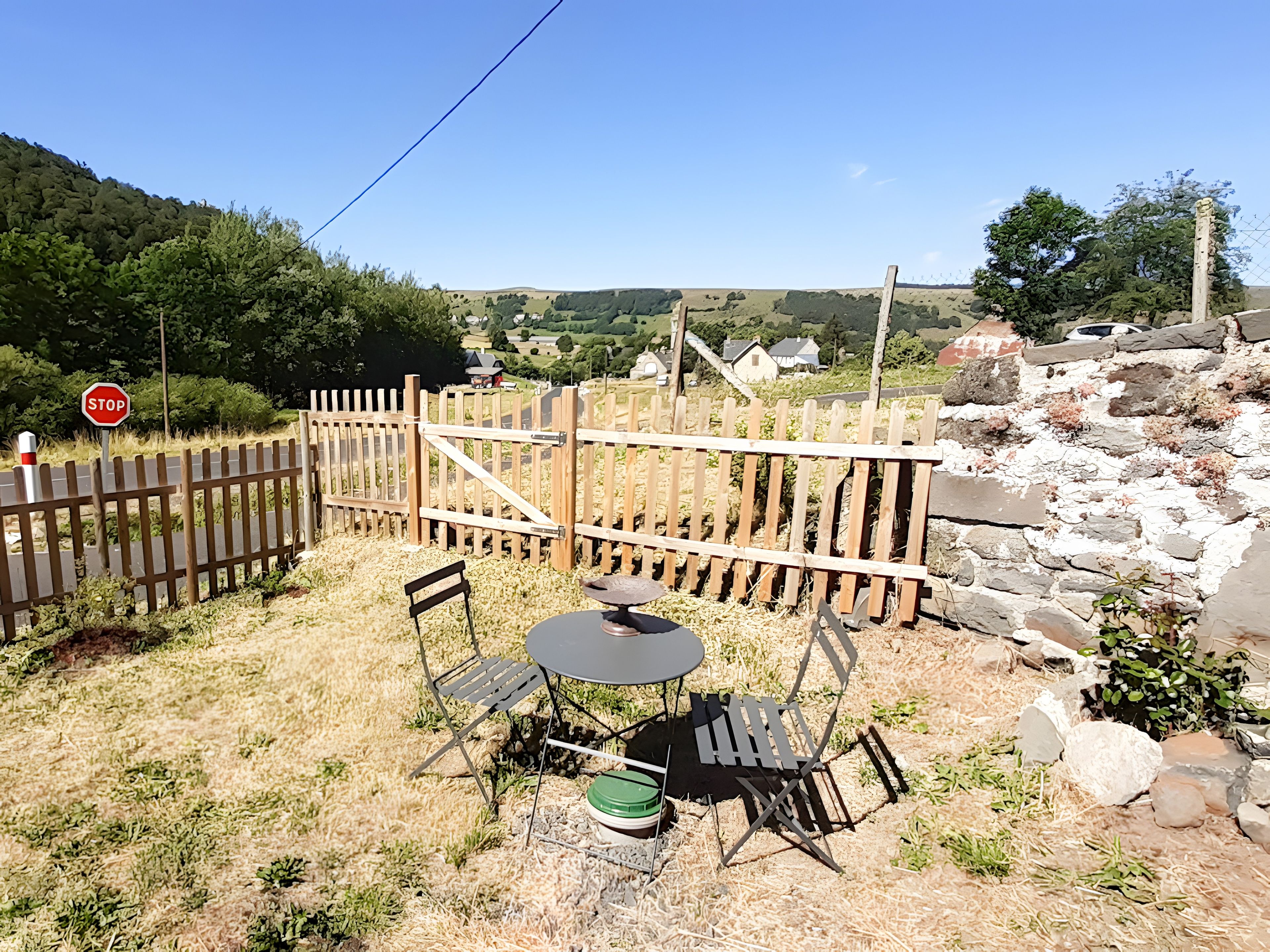 Área externa cercada com mesa e cadeiras, uma placa de pare e um muro de pedra.