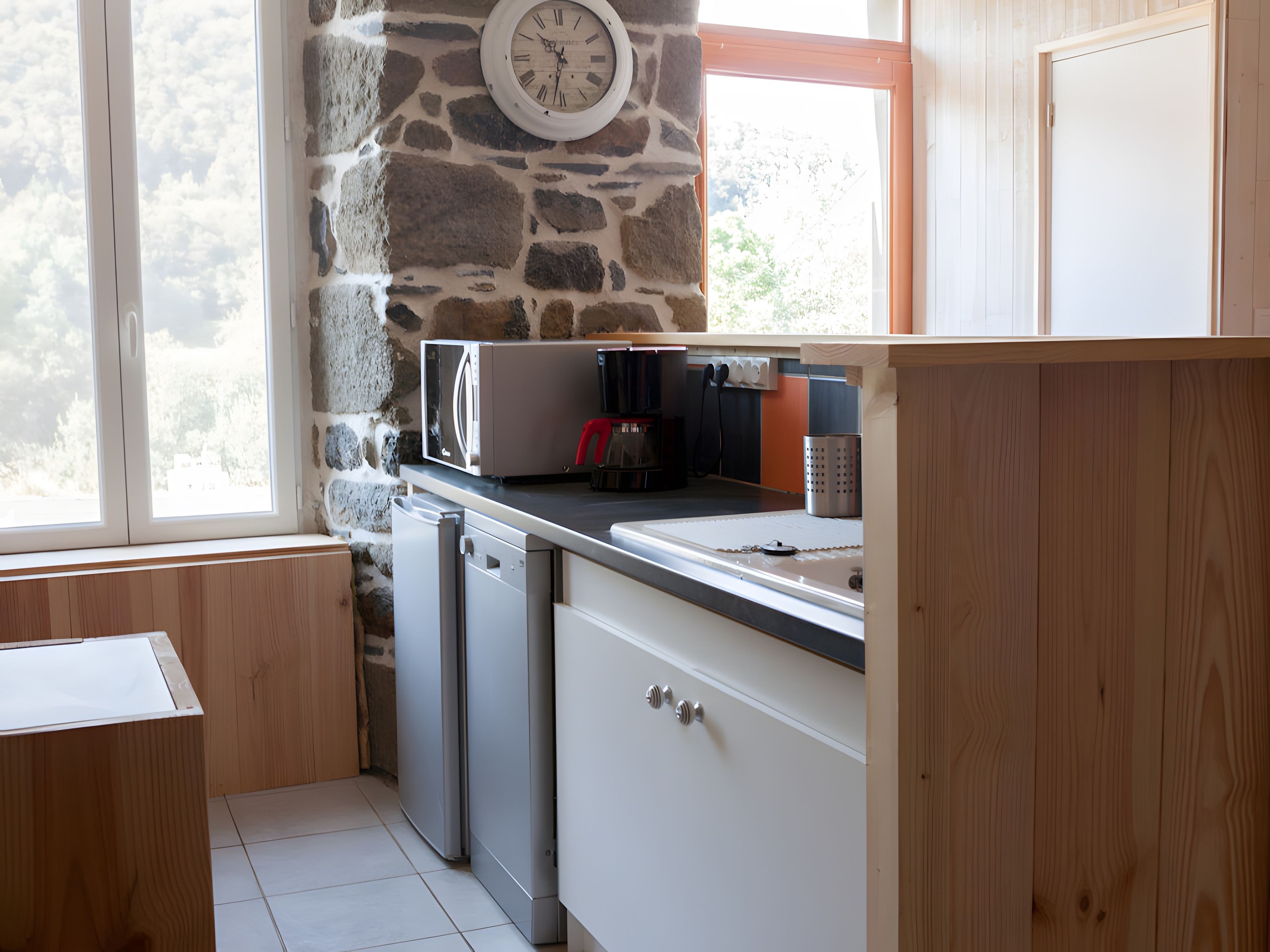 Una cocina con pared de piedra, un reloj, un microondas y un lavavajillas.