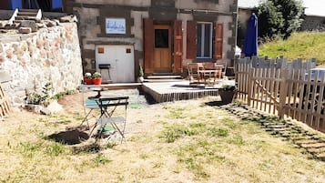 Een rustiek gebouw met een stenen gevel, houten luiken en een klein terras met een tafel en stoelen.