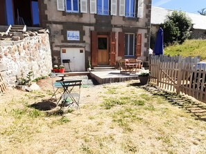 A rustic building with a stone facade, wooden shutters, and a small outdoor seating area with a table and chairs.