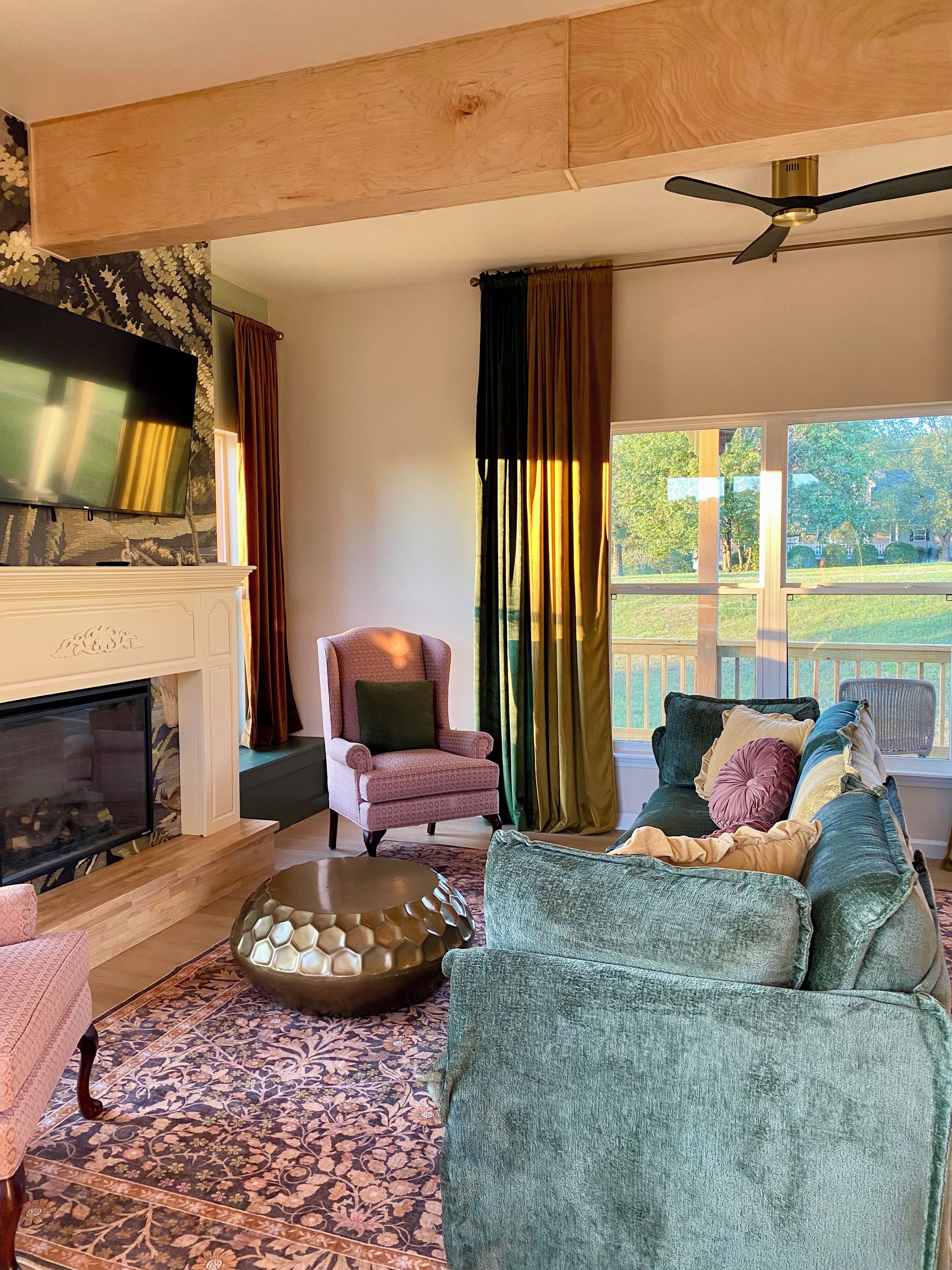 A living room with a fireplace, a television, a ceiling fan, and a view of the outdoors.