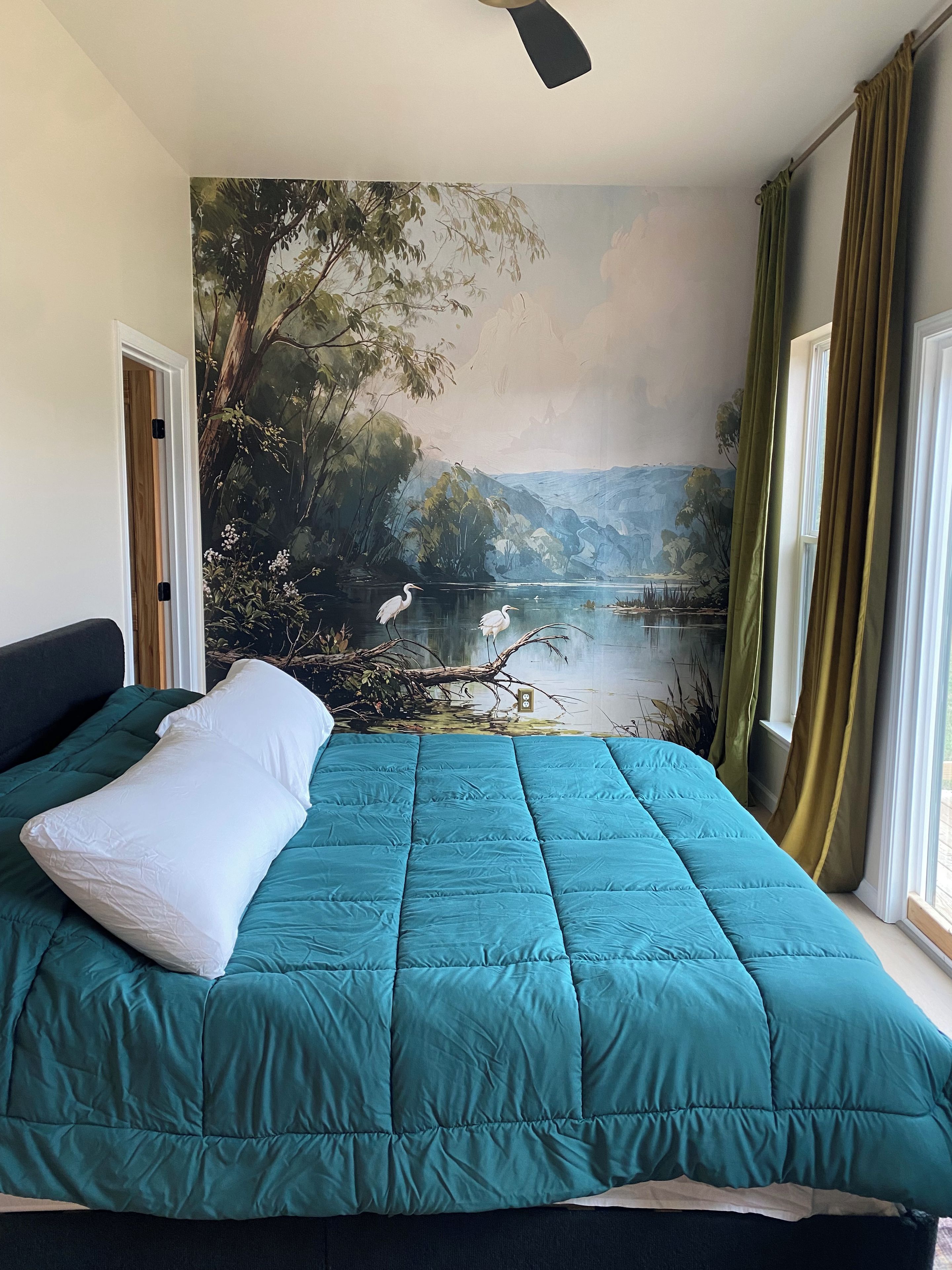 Un dormitorio con una cama grande, un mural de un paisaje y vista a un lago.