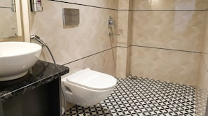 A bathroom with a white toilet, a sink with a black countertop, and a shower area with patterned tiles. - OnlyStay Veda Inn Ayodhya (Faizabad)