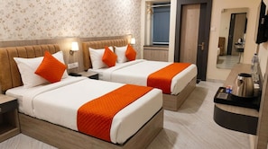 A hotel room with two beds, a bedside table, a nightstand, a mirror, a wooden floor, and a kitchenette area. - OnlyStay Veda Inn Ayodhya (Faizabad)