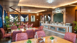 A restaurant with wooden paneling, pink velvet chairs, and a buffet counter with glassware. - OnlyStay Veda Inn Ayodhya (Faizabad)