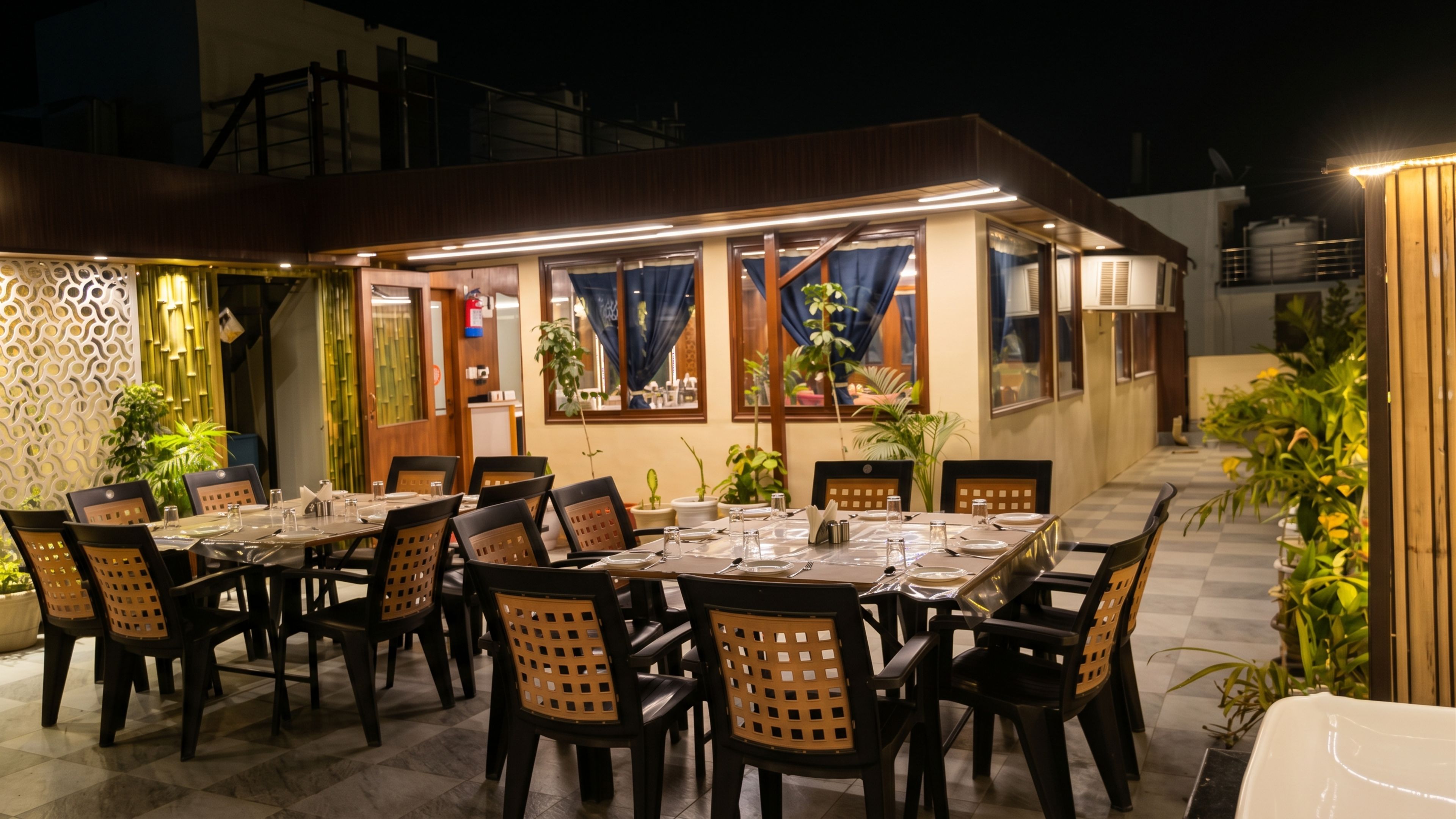 Un espace de restauration en plein air, avec des tables et des chaises, entouré de plantes et agrémenté d’un mur décoratif.