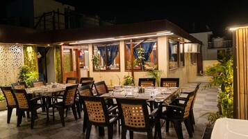 Un espace de restauration en plein air, avec des tables et des chaises, entouré de plantes et agrémenté d’un mur décoratif.