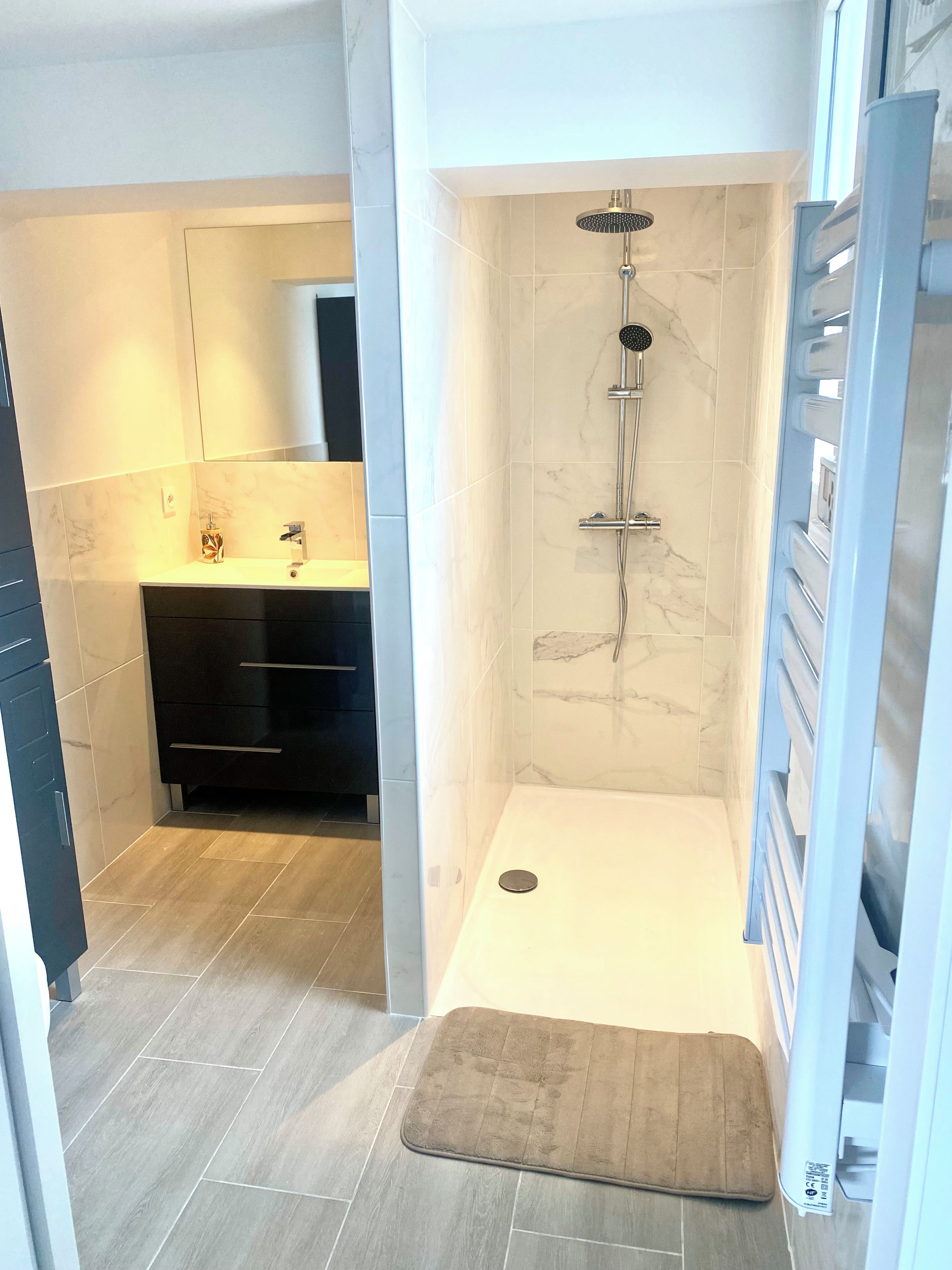 Une salle de bain moderne équipée d’une douche, d’un meuble-lavabo avec miroir et d’un porte-serviettes.