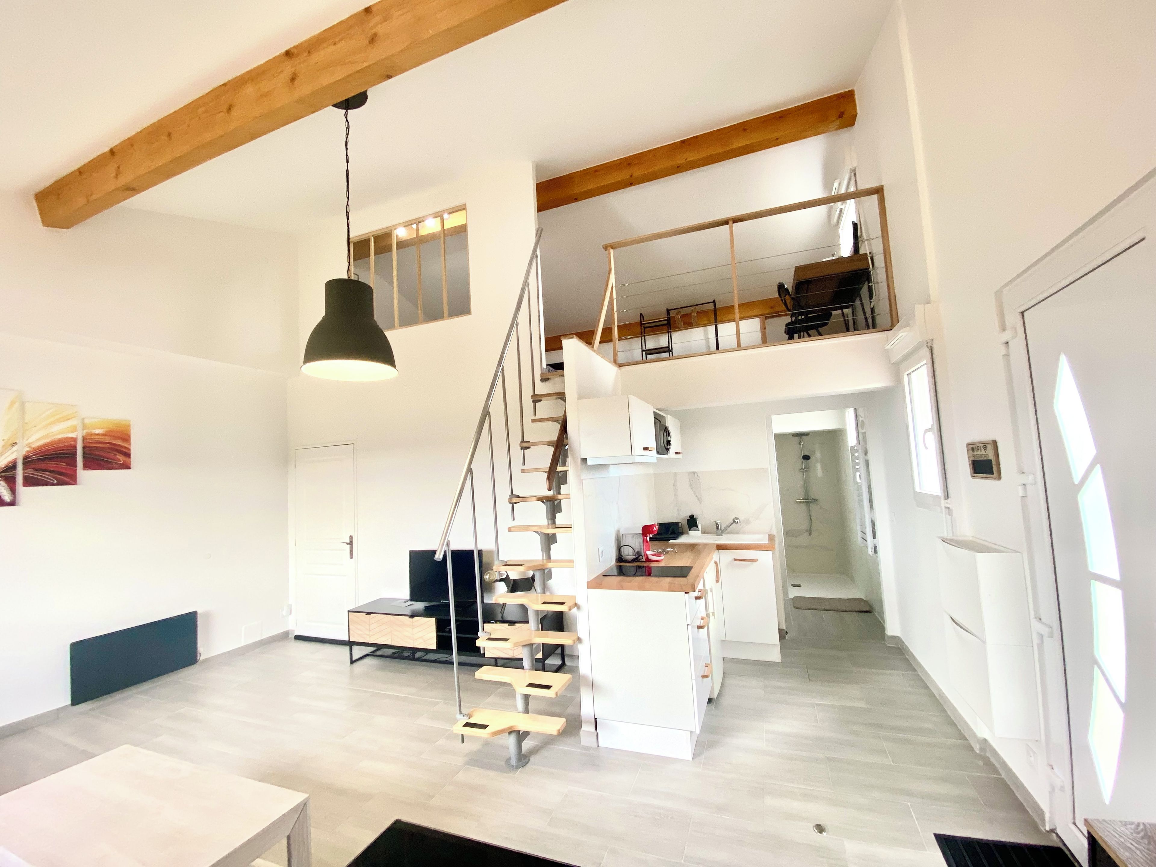 Ein geräumiges Loft mit hoher Decke, einer Treppe zu einer erhöhten Ebene und einer Küchenzeile.