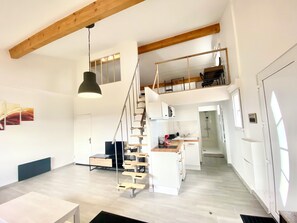 Ein geräumiges Loft mit hoher Decke, einer Treppe zu einer erhöhten Ebene und einer Küchenzeile.