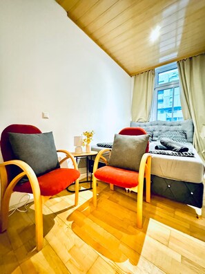A cozy room with two wooden chairs, a small table, a sofa, and a window with curtains. - A Little Vienna Private Room near FAC (Wien)