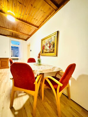 Ein Essbereich mit einem Holztisch, rot gepolsterten Stühlen und einem Blumenbild an der Wand.