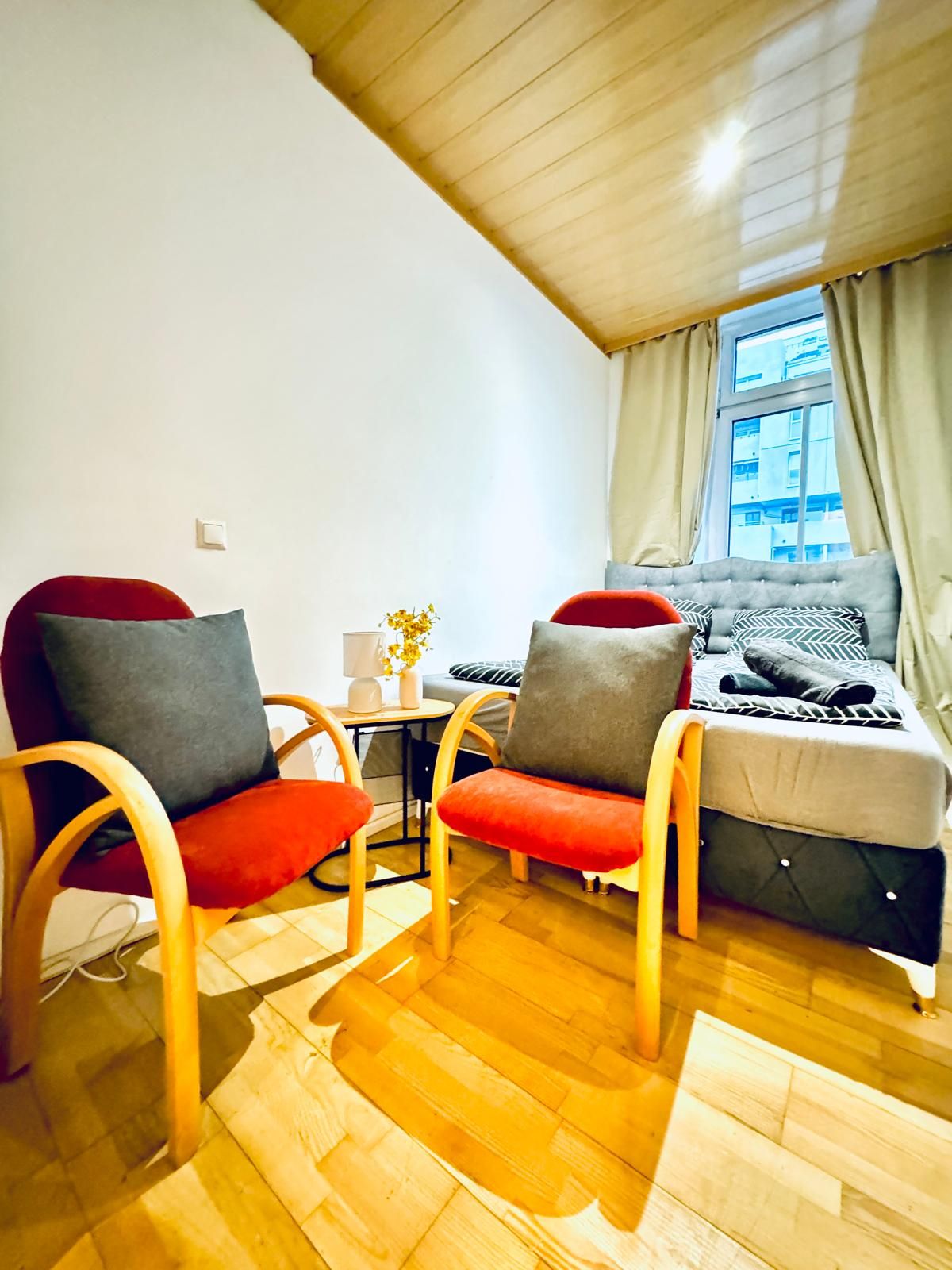 A cozy room with two wooden chairs, a small table, a sofa, and a window with curtains.