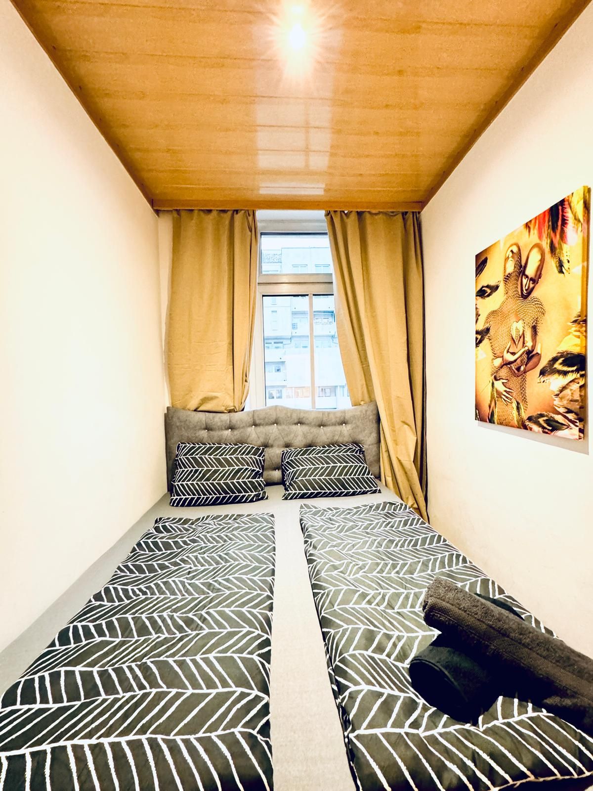 Una habitación pequeña con una cama, un ventanal con cortinas y un cuadro en la pared.