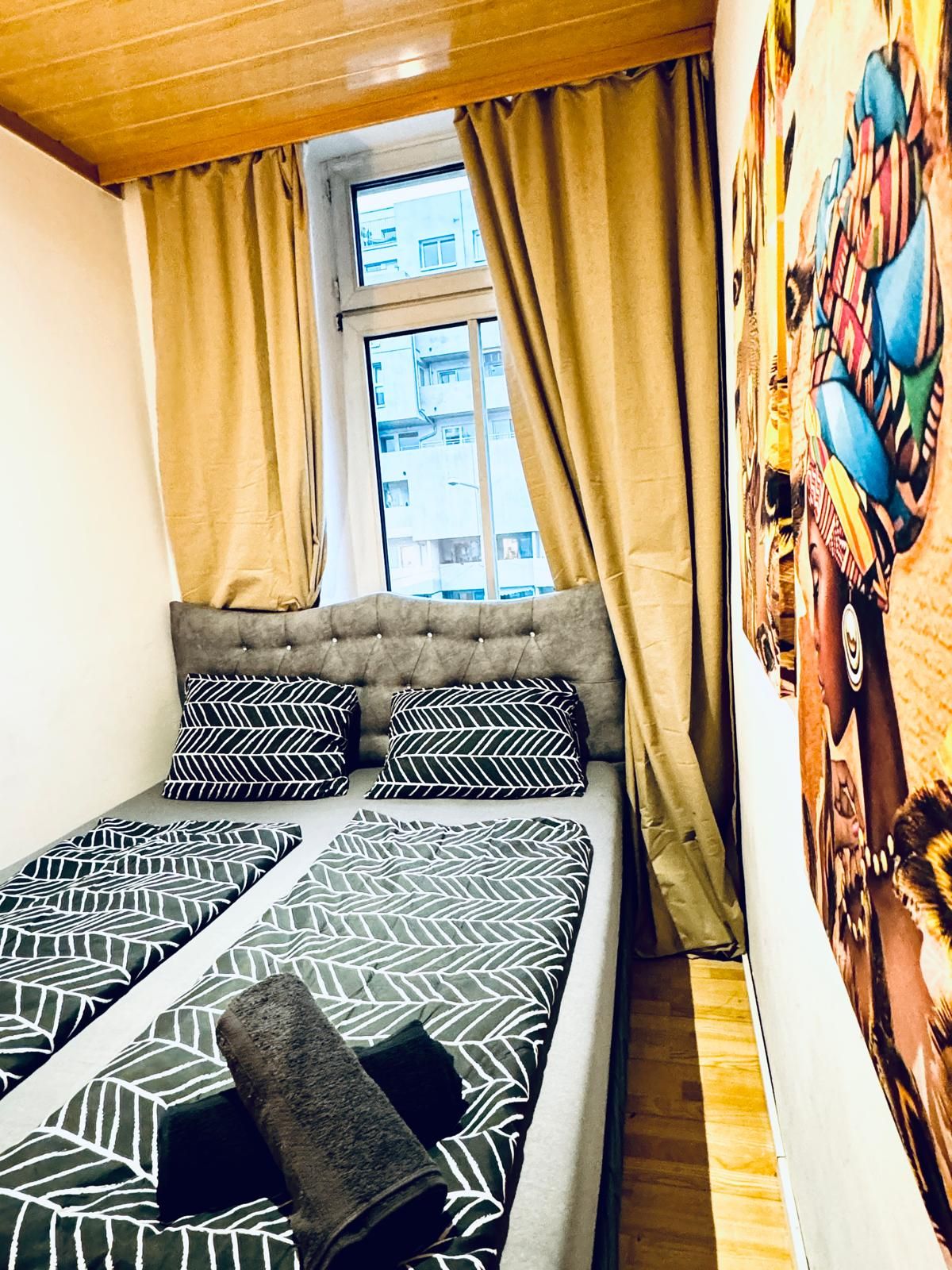 Una cama con ropa de cama estampada, una ventana con cortinas y una pared con un mural colorido.