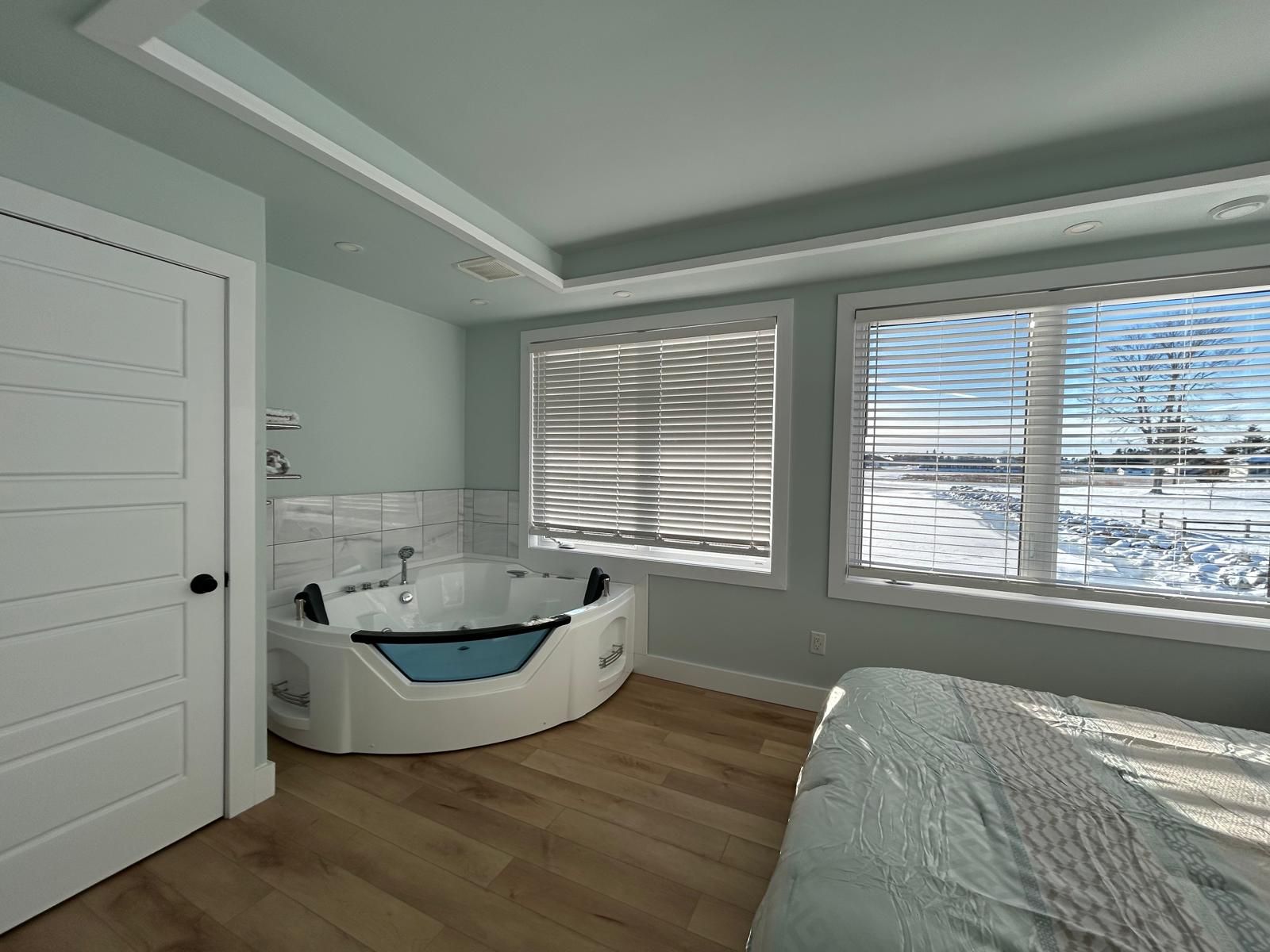 Un baño moderno con una bañera independiente, ducha y retrete. Hay ventanas amplias con persianas, y vistas a un paisaje nevado.