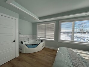 Un baño moderno con una bañera independiente, ducha y retrete. Hay ventanas amplias con persianas, y vistas a un paisaje nevado.
