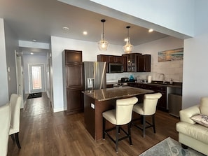A modern kitchen with dark wood cabinets, a stainless steel refrigerator, a microwave, and a large island with bar stools.