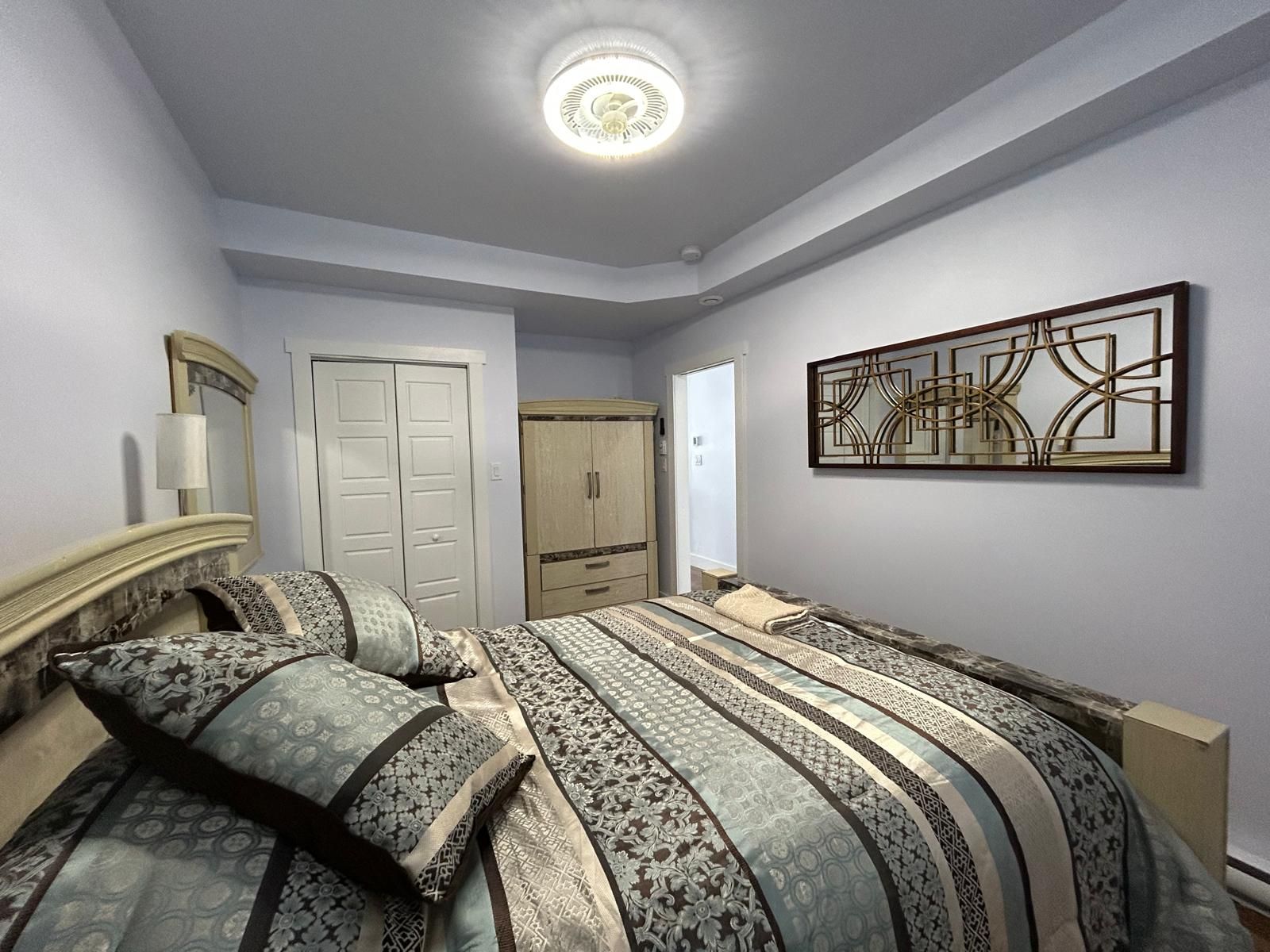 Un dormitorio con una cama, un armario, un espejo y una obra de arte en la pared.