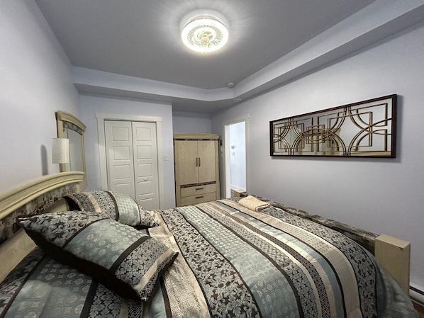 A bedroom with a bed, a wardrobe, a mirror, and a wall-mounted artwork.