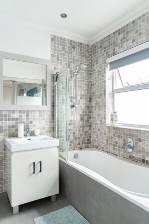A modern bathroom with a glass shower enclosure, a white vanity with a mirror, and a bathtub with a tiled surround.