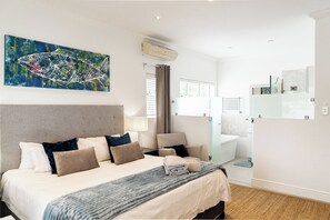 A hotel room with a bed, a bedside table, a lamp, a shower area, and a bathroom.