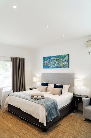 A modern bedroom with a large bed, bedside tables, a headboard, and a painting on the wall.
