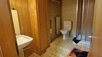 Un baño con tocador de madera, inodoro y zona de ducha.