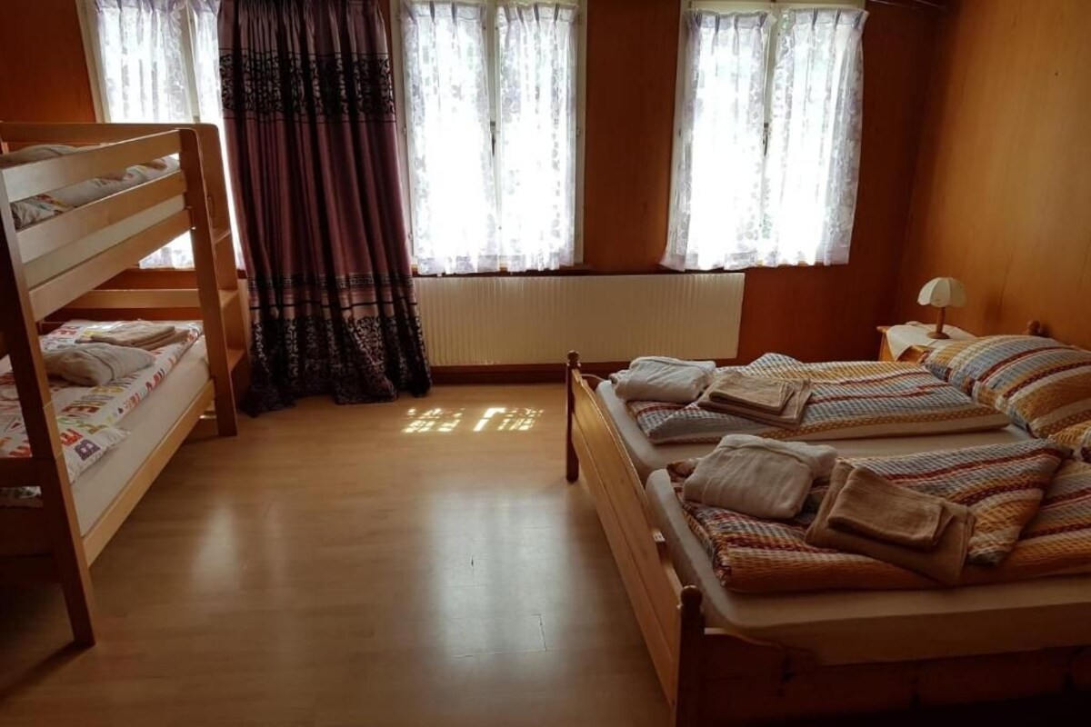 A room with a bunk bed, a single bed, a window with curtains, and a radiator.